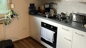 Eine moderne Küche mit weißen Schränken, einem eingebauten Backofen, einer Kaffeemaschine und einem Fenster mit Blick auf Grünflächen.