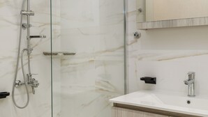 Une salle de bain moderne dotée d’une douche à parois de verre, d’un mur en marbre blanc, d’un meuble-lavabo en bois et d’un miroir avec éclairage intégré.