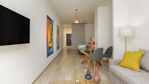 Un salon moderne doté d’un téléviseur à écran plat, d’un coin repas avec une table en verre et d’un canapé agrémenté d’un coussin jaune.