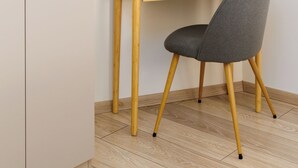 Une pièce au décor minimaliste, avec un bureau en bois, une chaise grise et un miroir rond accroché au mur.