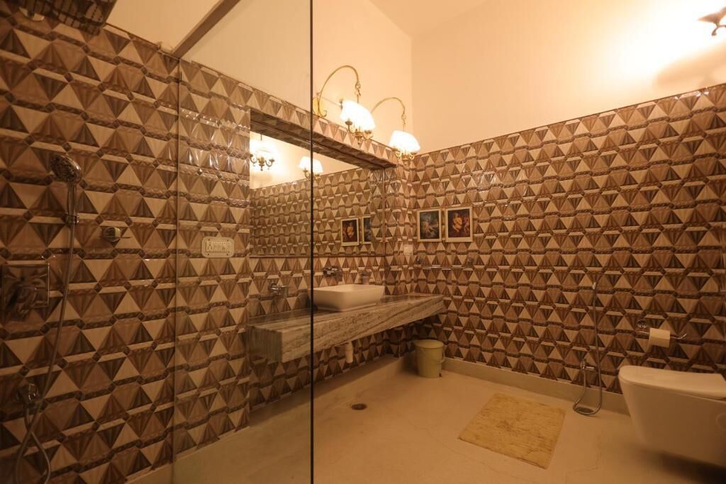 Un baño con pared de estampado geométrico, cabina de ducha de vidrio, lavamanos y retrete.