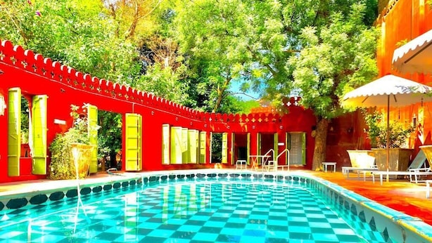 A pool with checkered tiles, surrounded by red and green structures, and trees in the background. - Partap Mahal (Bikaner)
