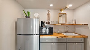 A compact kitchen with a stainless steel refrigerator, a microwave, a sink, and a wooden countertop.