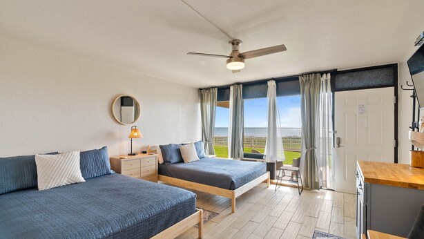 A bedroom with two beds, a ceiling fan, a window with curtains, and a view of the outdoors.