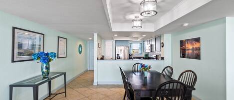 A dining area with a dark wooden table and chairs, a vase with flowers, and a light blue wall.