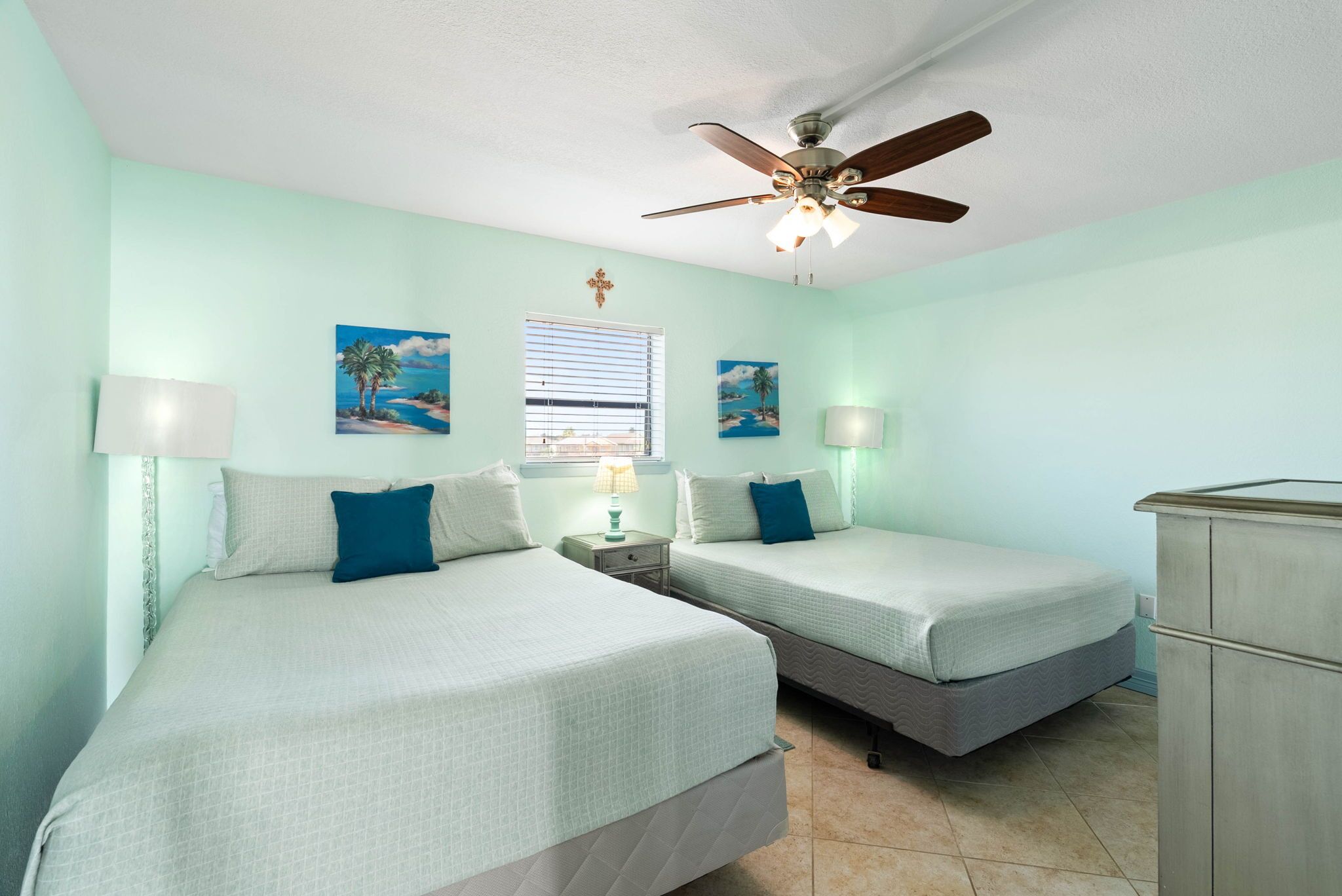 A room with two beds, a ceiling fan, and artwork on the walls.