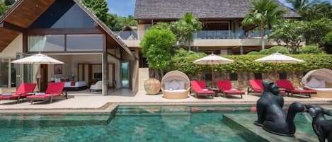 A resort with a pool, red lounge chairs, and a large building with a sloped roof.
