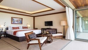 A hotel room with a large bed, a television, a desk, and a view through a glass door.