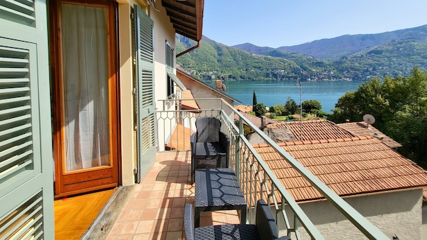 Un balcon avec vue sur un lac et des montagnes, une porte en bois et un sol carrelé.