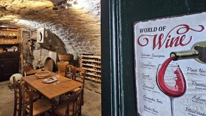 Une cave rustique avec une table et des chaises en bois, des étagères à vin et un menu affiché au mur, présentant une sélection de vins.