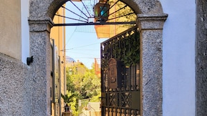 Une entrée en pierre en forme d’arc surmontée d’un portail en métal, un pot de fleurs et un panneau portant le chiffre « 12 » fixé au mur.