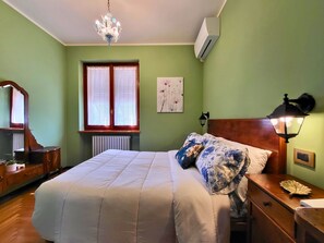 A bedroom with a bed, a dresser, a nightstand, a lamp, a radiator, and a window with curtains. - Jasmine House, Laglio, Lake Como (Laglio)