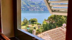 Une fenêtre donnant sur un lac, une végétation luxuriante et une chaîne de montagnes lointaine.