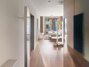 A modern hotel room with a wooden floor, a bed with white bedding, and a view of the outdoor balcony.