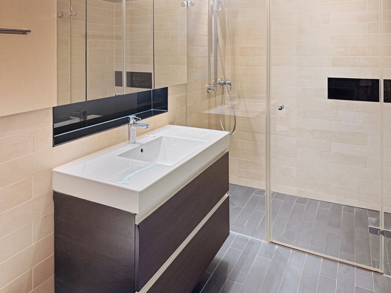 Une salle de bain moderne avec un grand miroir, un lavabo blanc et un espace douche.