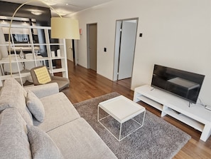 A modern living room with a grey sofa, a white coffee table, a flat-screen TV on a white stand, and a grey shaggy rug.