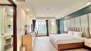 A hotel room with a large bed, a desk with a chair, a small trash bin, and a window with curtains. - LAGUNA Premier Hotel (Ho Chi Minh City)