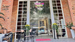 A building entrance with a large glass door, a brick facade, and a balcony with metal railings. - LAGUNA Premier Hotel (Ho Chi Minh City)