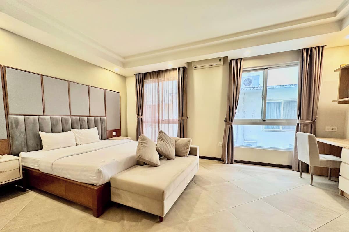 A modern hotel room with a large bed, a sofa, a desk, and a view of the city through the windows.