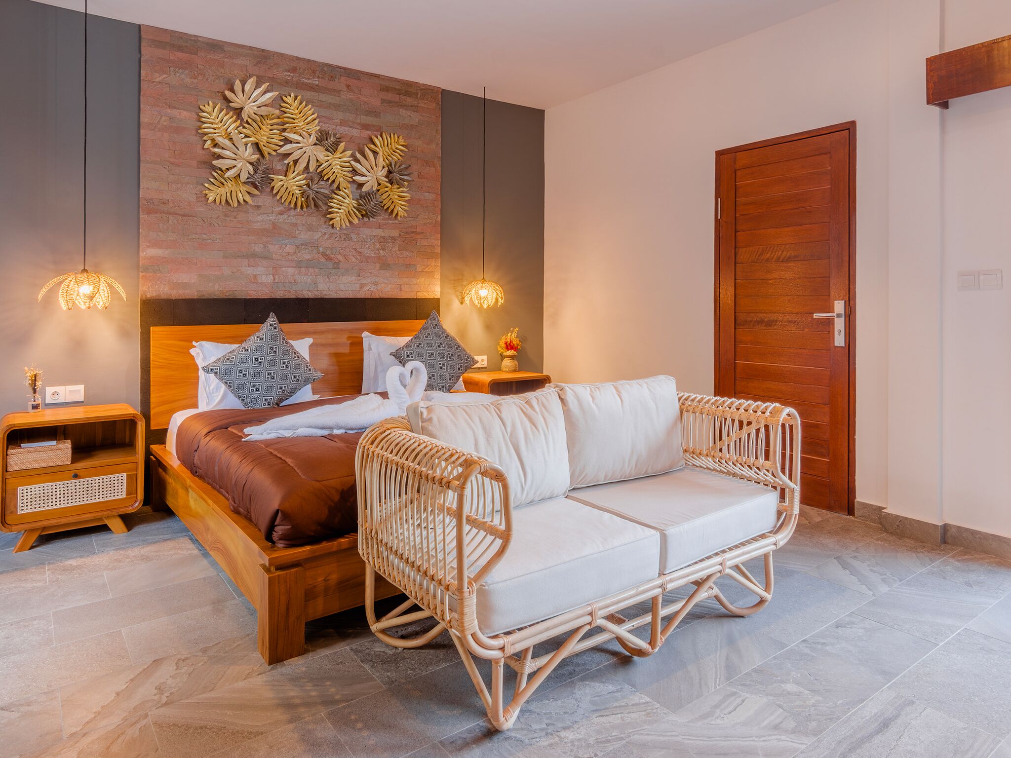 A bedroom with a wooden bed, a wicker sofa, a wall-mounted decorative piece, and a wooden door.