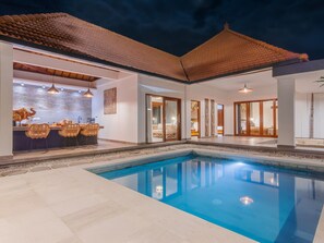A modern pool area with a clear blue pool, a bar area with wicker chairs, and a spacious living area with sliding glass doors. - villa dunia lembongan (Lembongan Island)