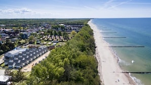 An aerial view of a coastal area with a beach, a row of houses, and a forested area. - Collins Holiday (Sianożęty)