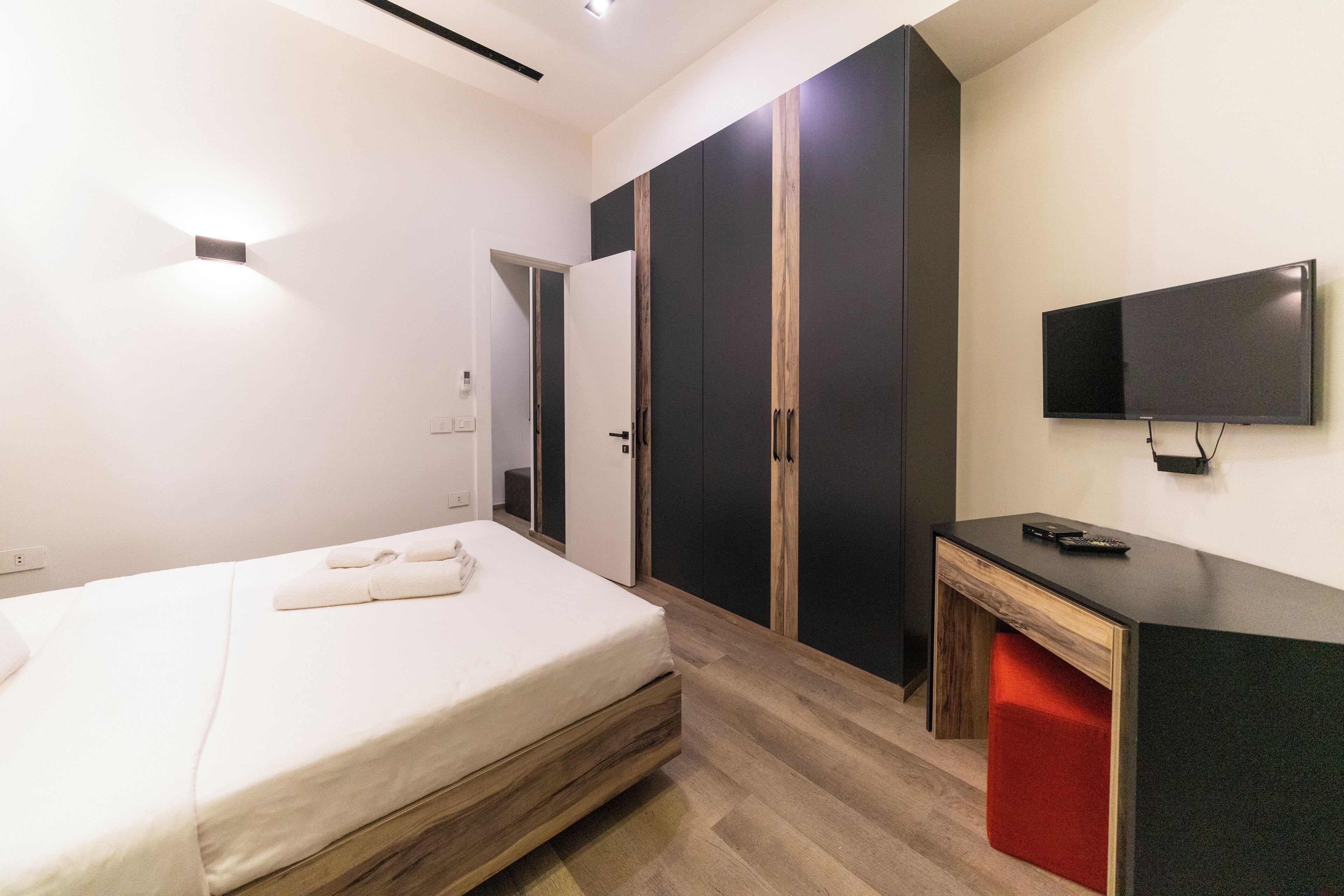A modern hotel room with a bed, wardrobe, desk, and TV.
