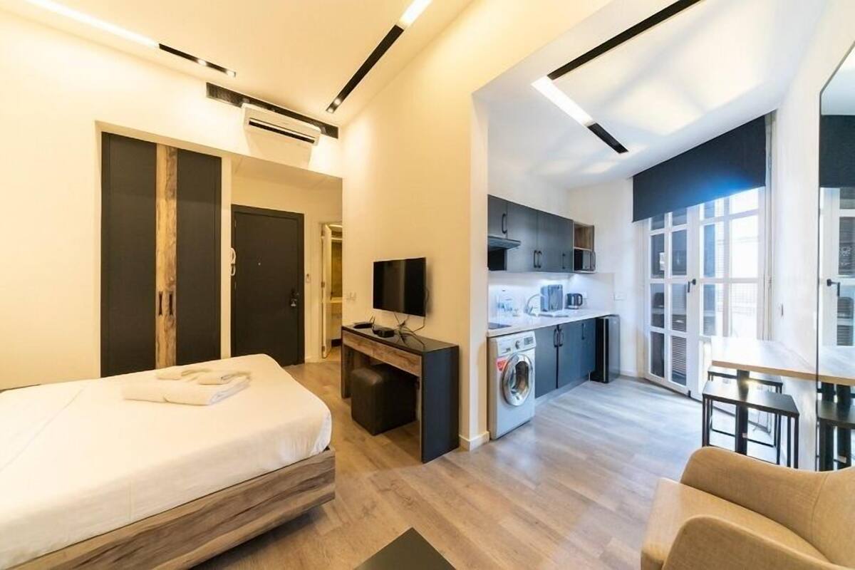Une chambre d’hôtel moderne équipée d’un lit, d’un bureau, d’une télévision, d’une machine à laver et d’un coin repas.
