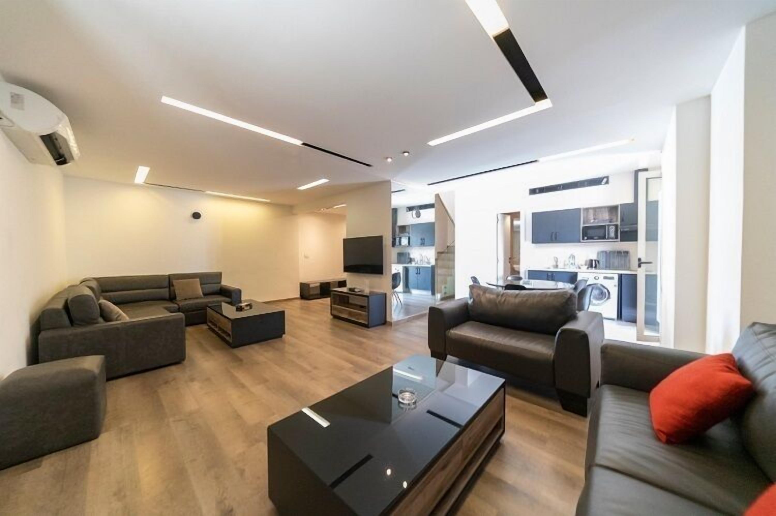 A modern living room with a sectional sofa, a glass coffee table, and a kitchen in the background.