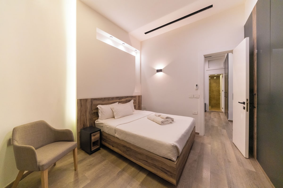 Une chambre à coucher moderne avec un lit en bois, une table de chevet, une chaise et une armoire.