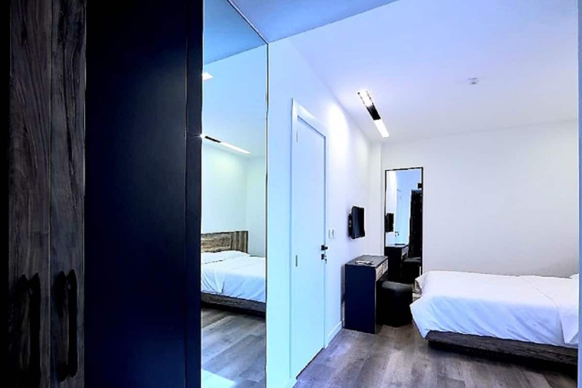 Une chambre d’hôtel moderne, dotée d’un grand miroir, de deux lits, d’un bureau et d’une armoire.