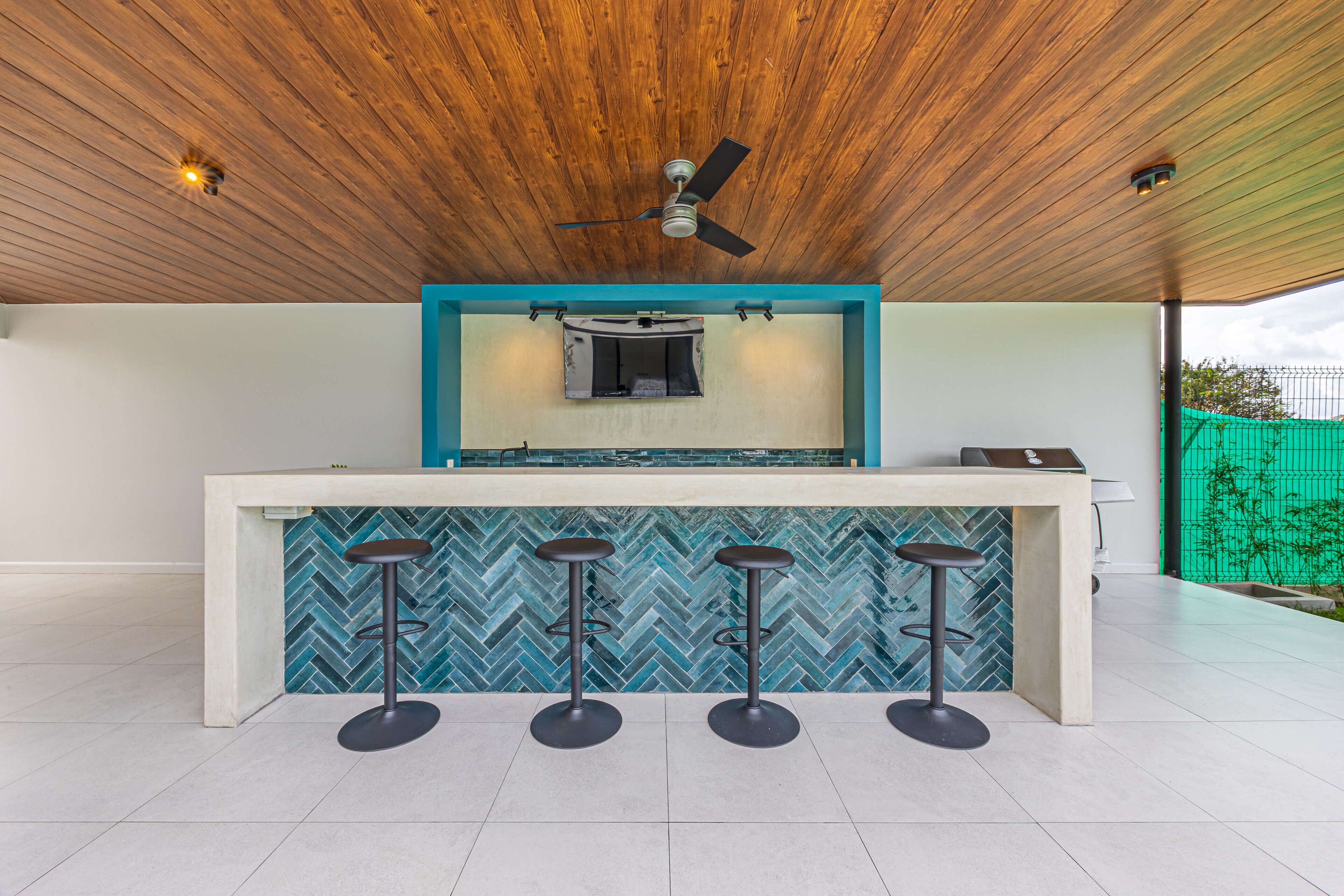 Een keuken met een houten plafond, een plafondventilator, een backsplash van visgraatmozaïek en drie barkrukken.