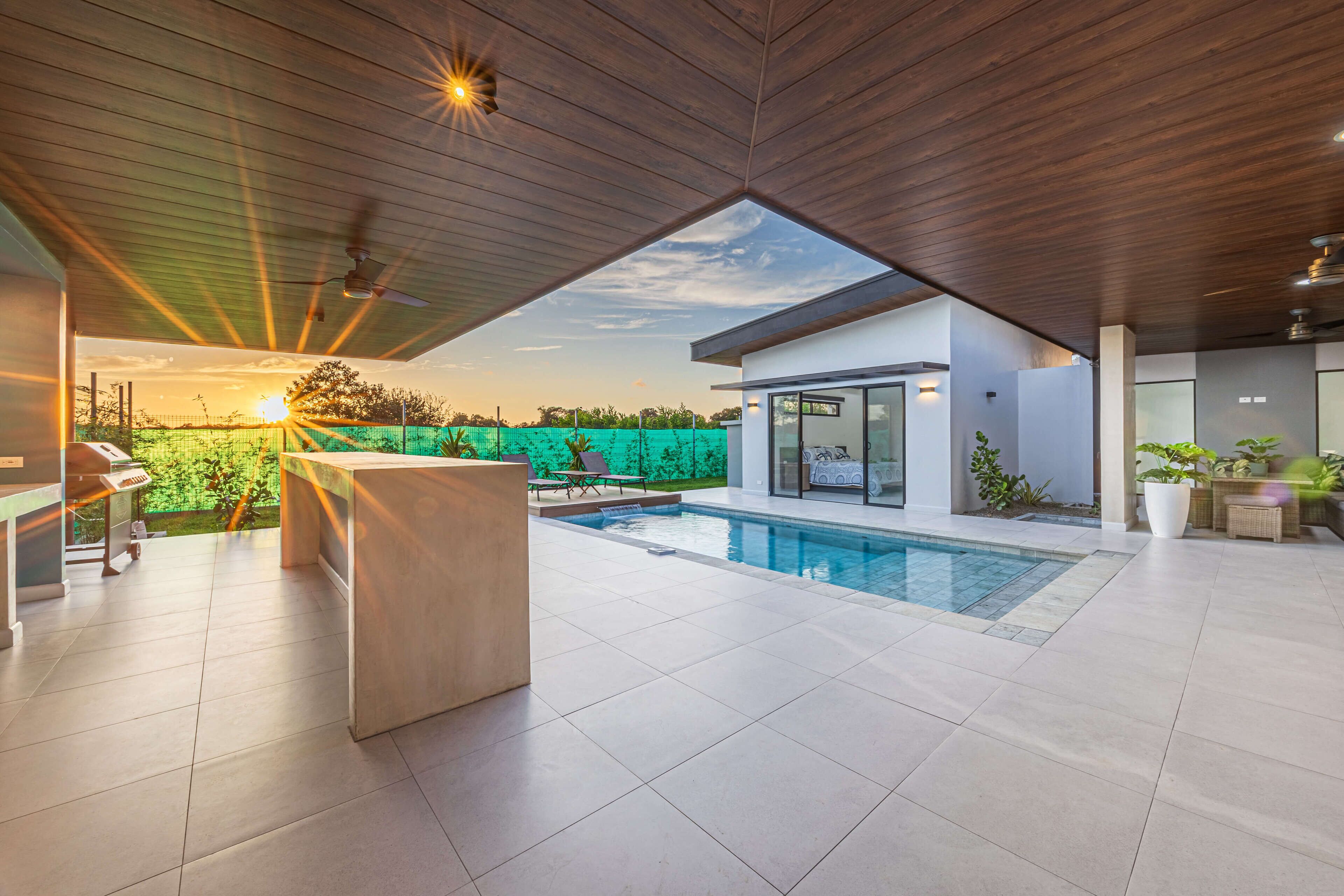 Ein moderner Poolbereich im Freien mit Holzboden, einer Bar und Blick auf den Sonnenuntergang.