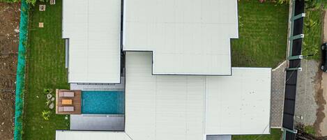 Vista aérea de um edifício moderno com várias seções, piscina e área cercada.
