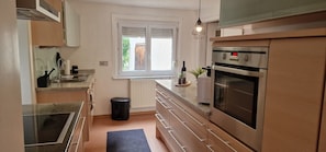 A modern kitchen with a built-in oven, a window, and a black trash bin. - Apartment 'M B Homes Schlatt' with Shared Garden, Wi-Fi, Parking (Hechingen)