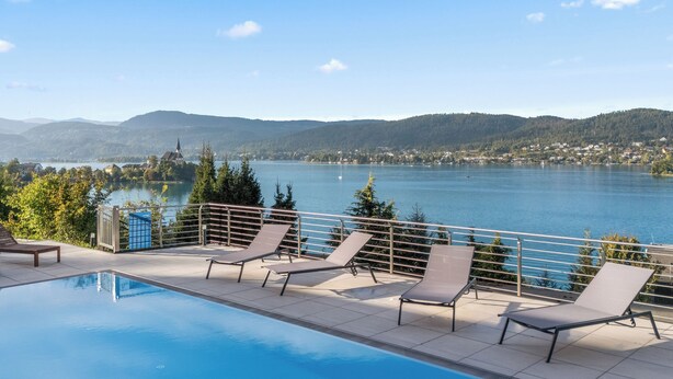 A pool area with lounge chairs and a view of a lake and mountains. - Maria Blick Lake View Apartments (Maria Woerth)