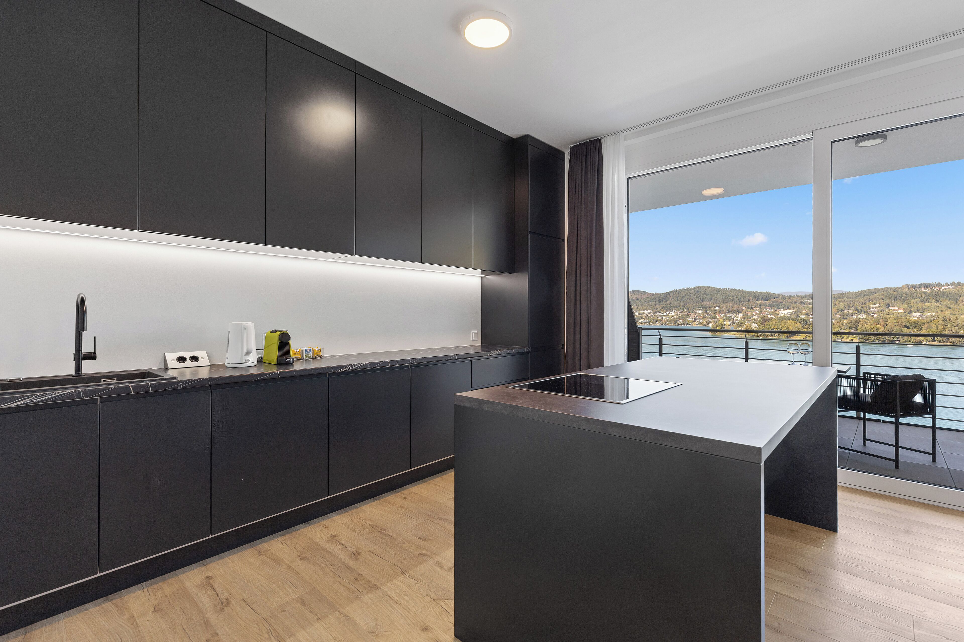 A modern kitchen with dark cabinetry, a central island, and a view of a lake and hills.