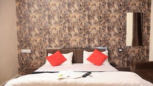 A neatly made bed with white bedding and red pillows, a remote control, and a smartphone on the bed.