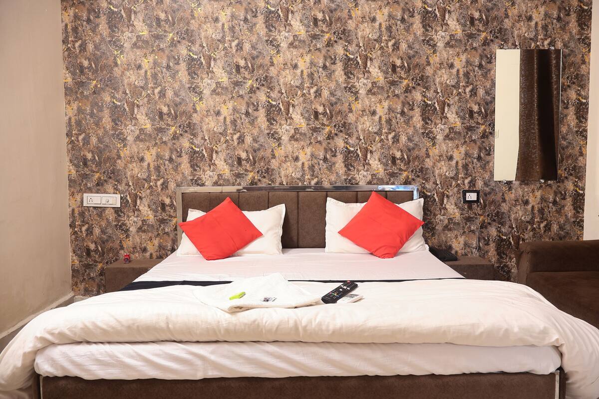 A neatly made bed with white bedding and red pillows, a remote control, and a smartphone on the bed.