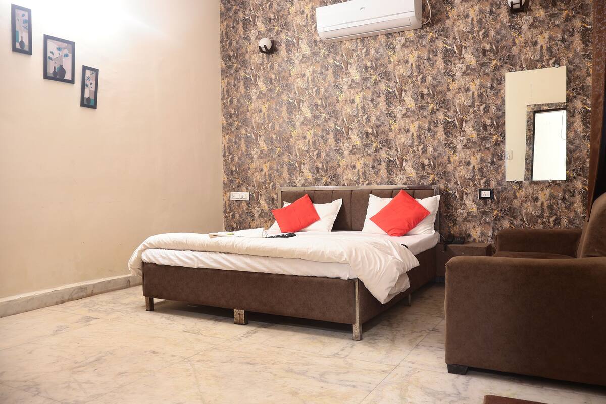 A bedroom with a bed, a chair, a wall-mounted air conditioner, and a textured wall.