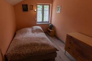 Un dormitorio con cama, cómoda, una mesita con un globo terráqueo, ventana con cortinas y decoración en la pared.