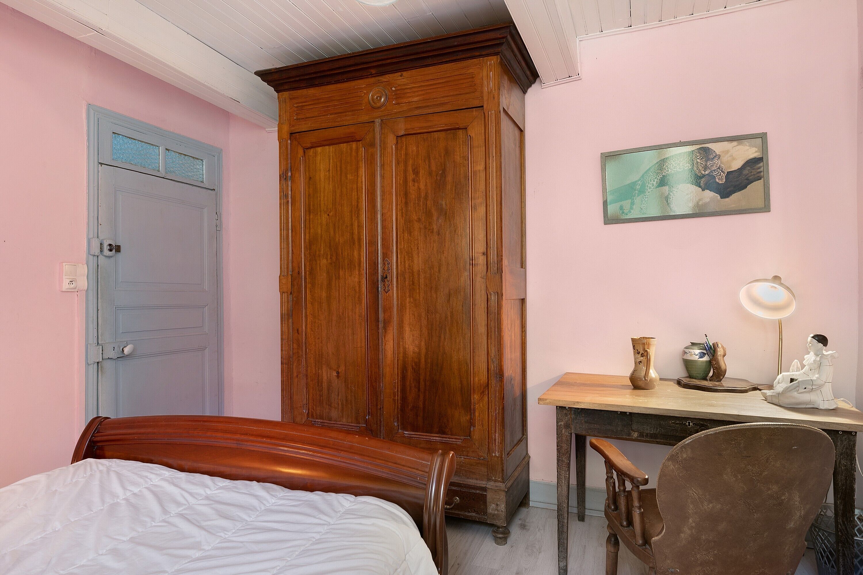 Un dormitorio con una cama, un armario de madera, un escritorio con una silla y un cuadro en la pared.
