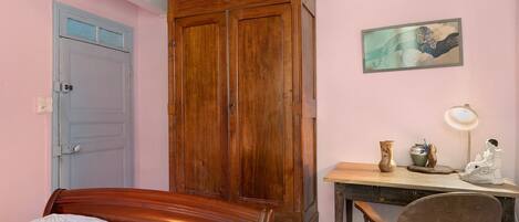 Un dormitorio con una cama, un armario de madera, un escritorio con una silla y un cuadro en la pared.