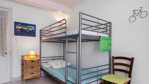 Habitación con literas, una toalla verde, una mesita de mimbre con una lámpara y una silla de madera.