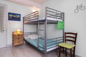 Habitación con literas, una toalla verde, una mesita de mimbre con una lámpara y una silla de madera.