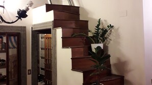 Un escalier en bois avec un radiateur en bas, une plante en pot sur la plateforme et une petite fenêtre dans le mur.