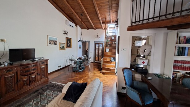 Un vaste salon doté d’un plafond en bois, d’un canapé, d’une table à manger et d’un escalier menant à un niveau supérieur.
