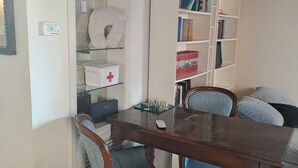 Un coin repas comprenant une table en bois, deux chaises rembourrées, une bibliothèque et un meuble blanc orné d’une croix rouge.