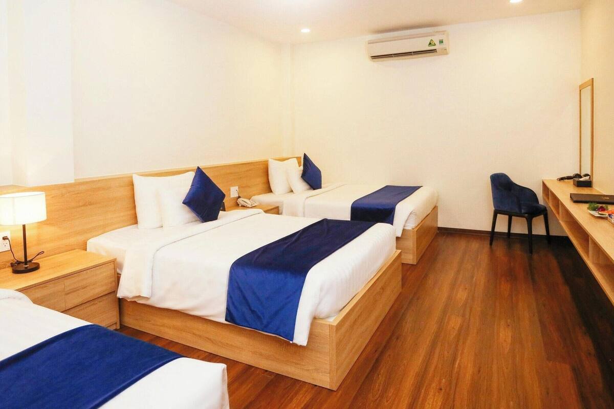 A hotel room with two beds, a desk, a chair, a TV, and an air conditioning unit.