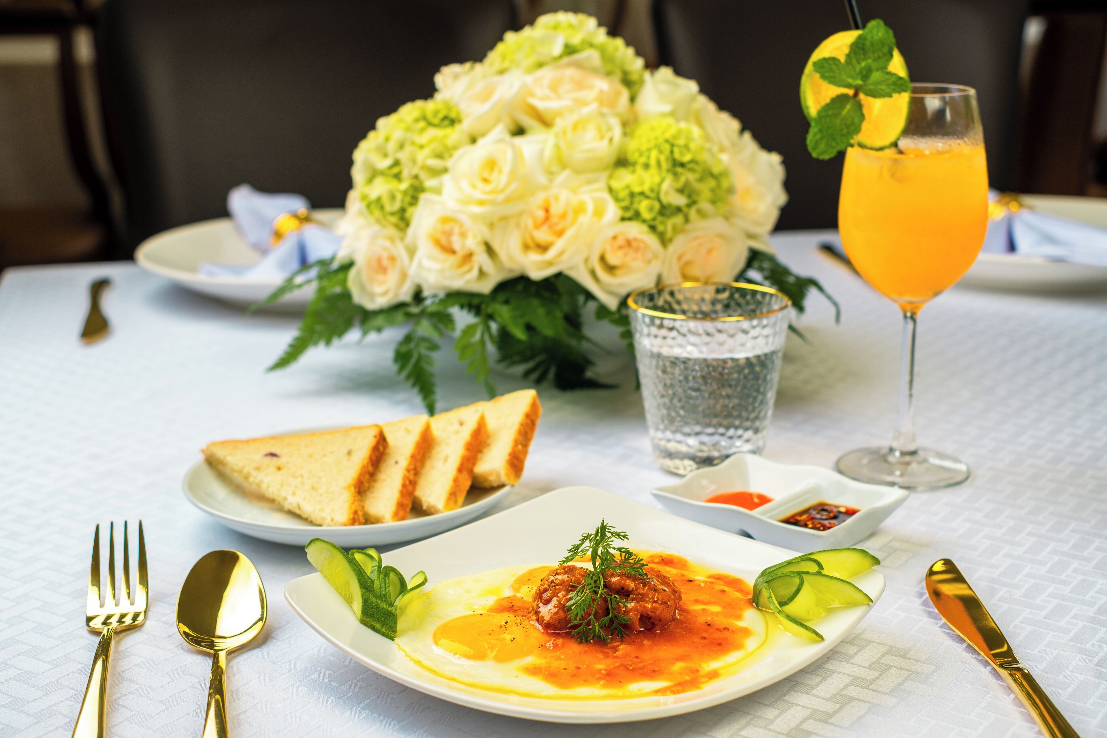 Ein Esstisch mit einem Teller Essen, einem Glas Orangensaft, einem Strauß weißer Rosen und einem Glas Wasser.